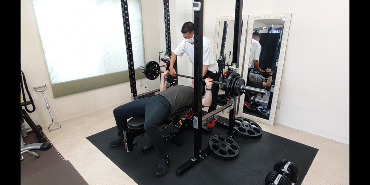 トレーナーの補助を受けながらベンチプレスを行うお客様
