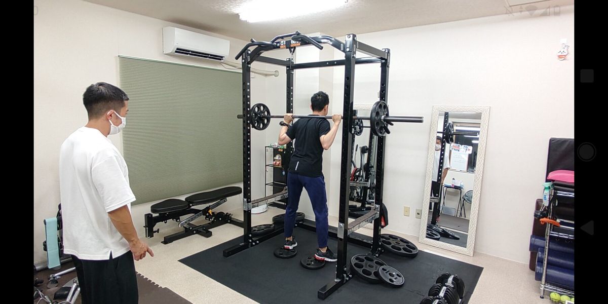 パワーラックを使うお客様へトレーナーが声をかける様子