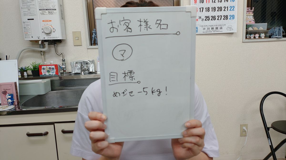 女性のお客様がマイナス5キロの目標を書いたホワイトボードを掲げる様子