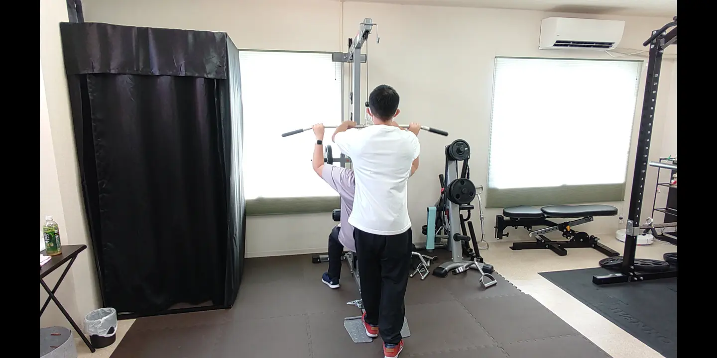 トレーナーがラットプルダウンのフォームをサポートする様子